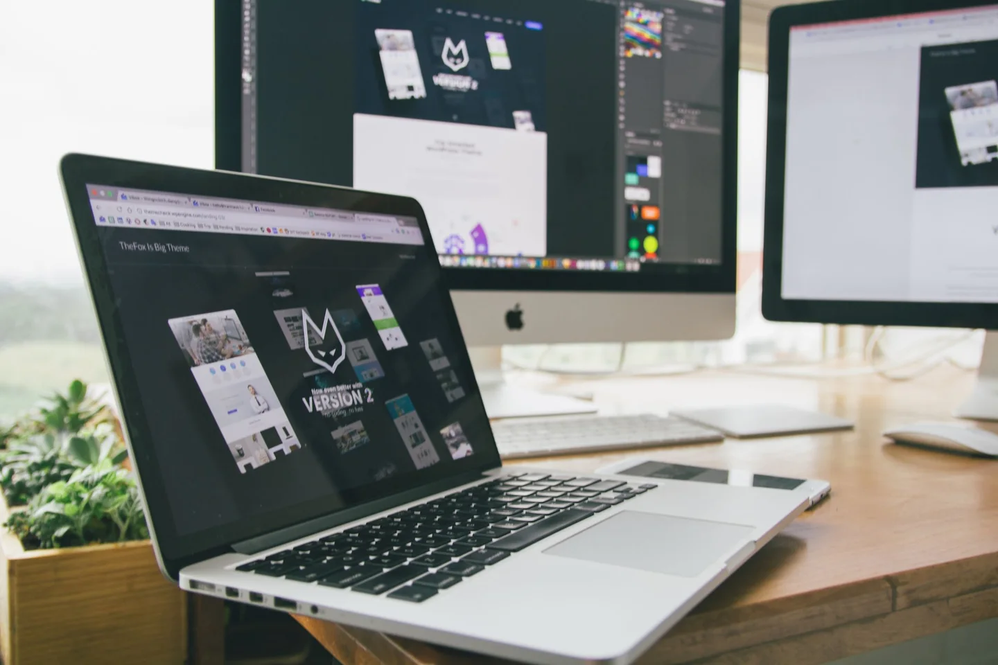 A website designer reviewing responsive page layouts across a laptop and external displays.