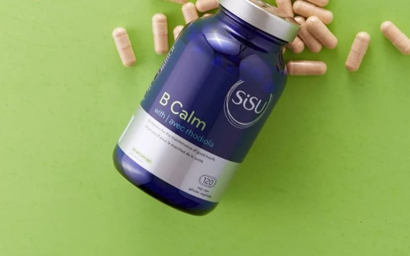A SISU B calm supplement bottle surrounded by capsules on a green surface.
